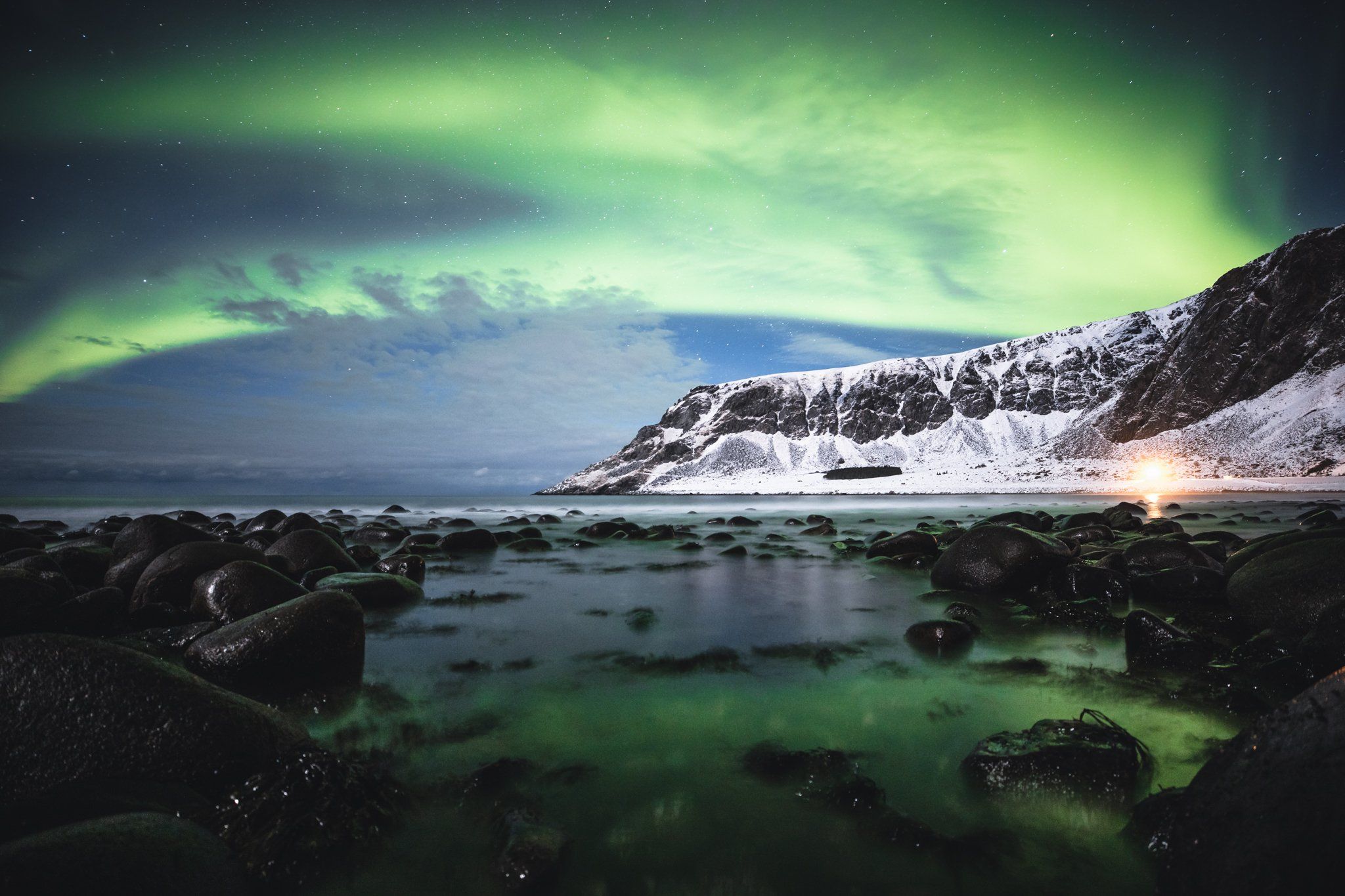 The Northern lights illuminate the sky, casting green reflections in the lake below.
